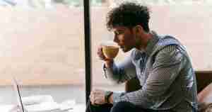 man drinking coffee and looking at laptop